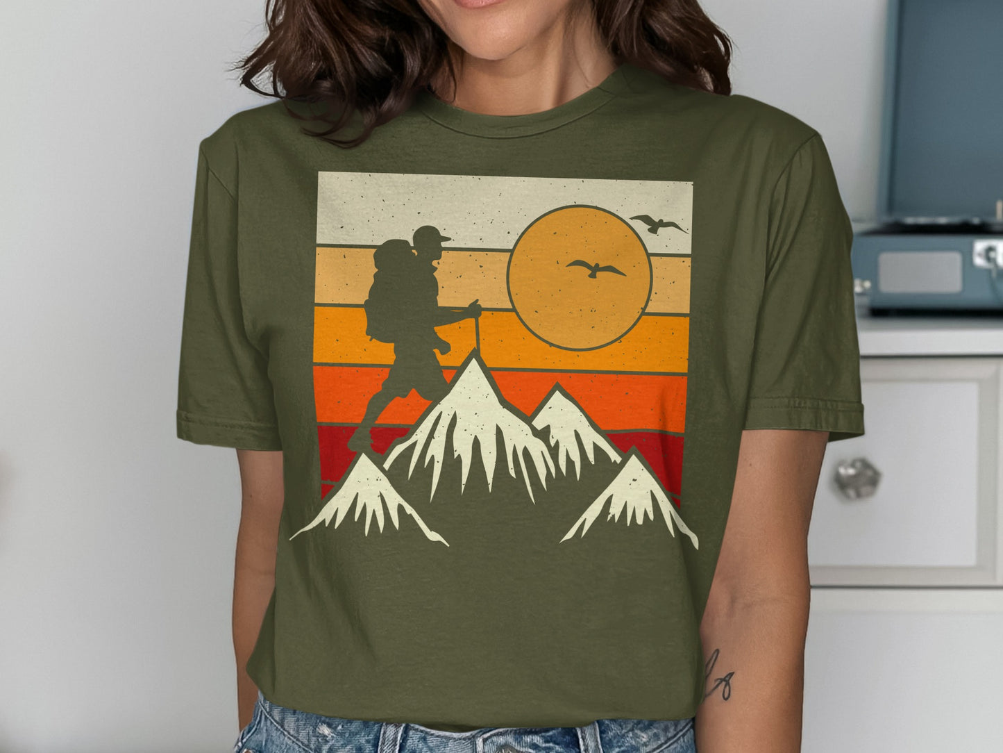 Hiking silhouette against a sunset with mountains and birds.
