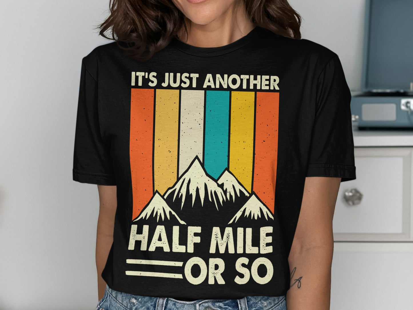 Black t-shirt with retro mountain graphic and text "IT'S JUST ANOTHER HALF MILE OR SO".