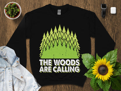 Black sweatshirt with green pine trees and "The Woods Are Calling" text.