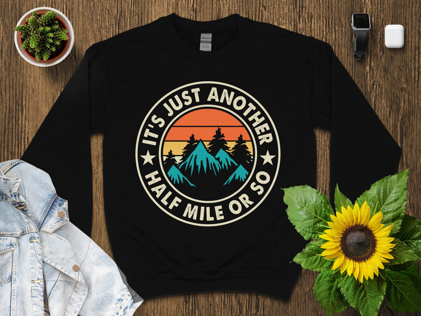 Black sweatshirt with round graphic of mountains, sun, and text "IT'S JUST ANOTHER HALF MILE OR SO".