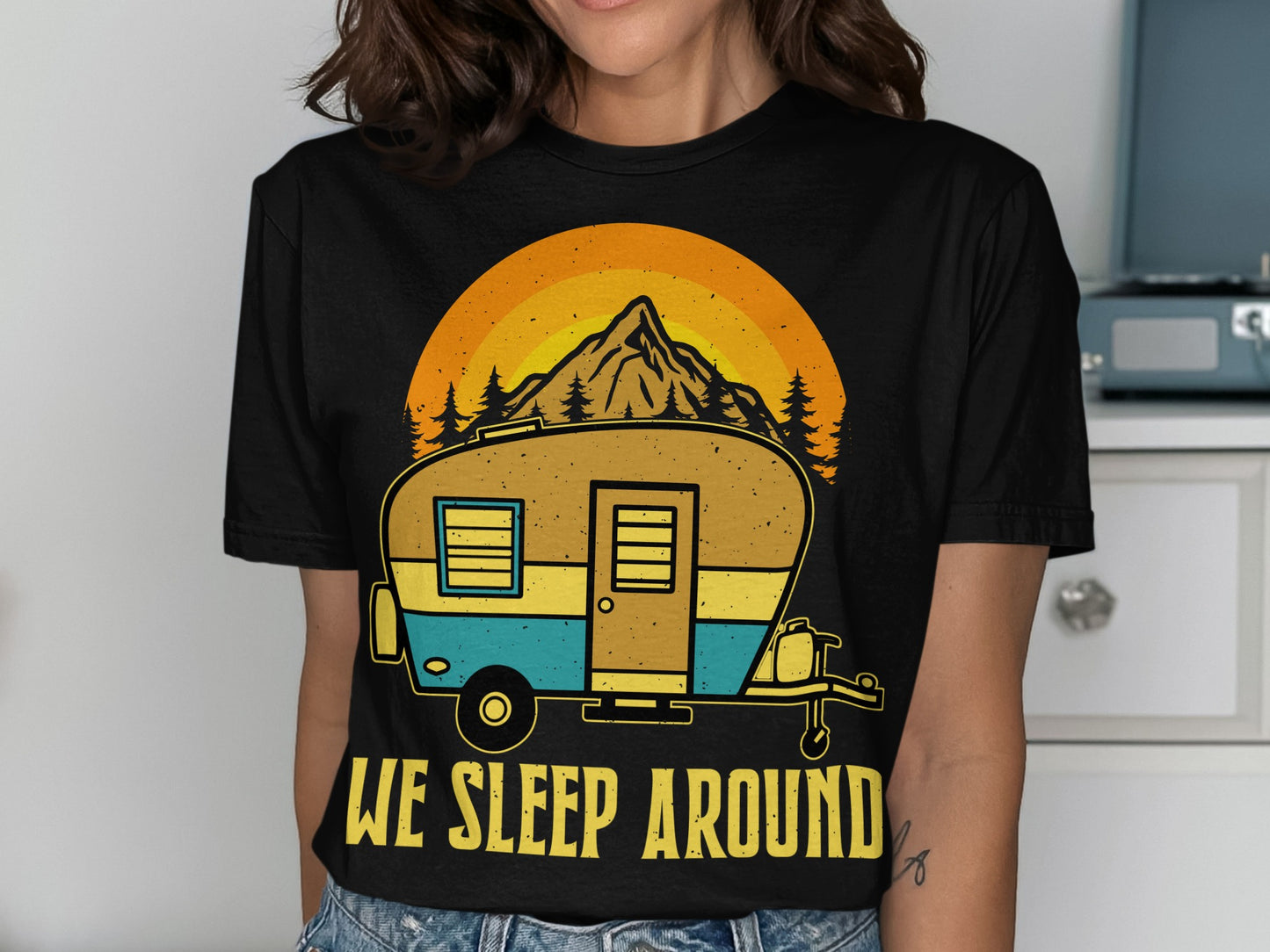 Black t-shirt with a graphic of a camper, mountain, and trees, and text "WE SLEEP AROUND".