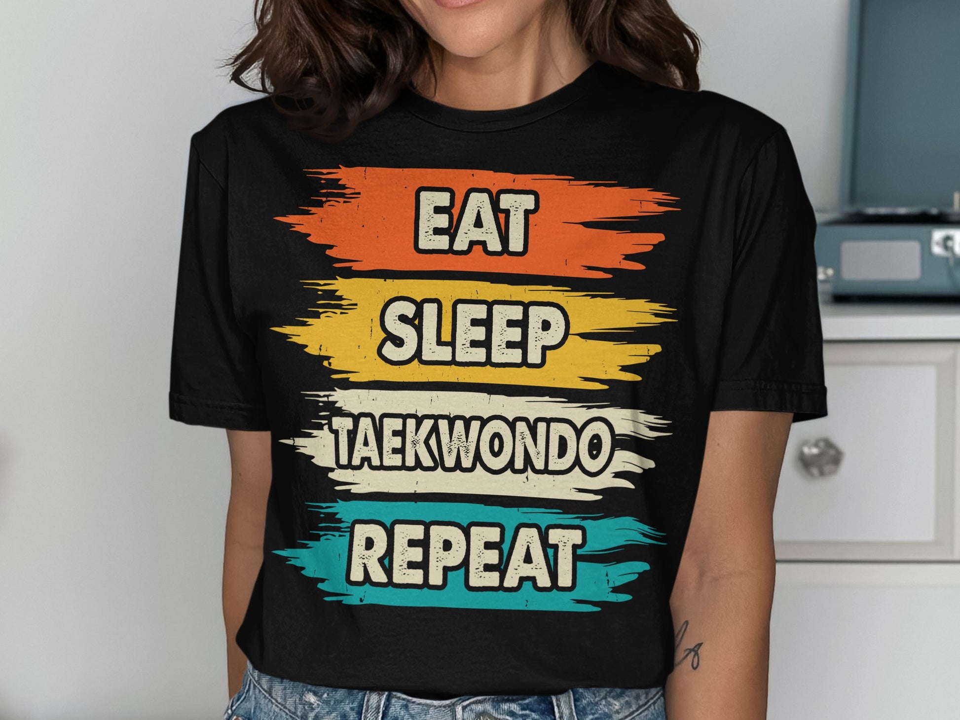 Black t-shirt with "EAT SLEEP TAEKWONDO REPEAT" text in colorful brush strokes.