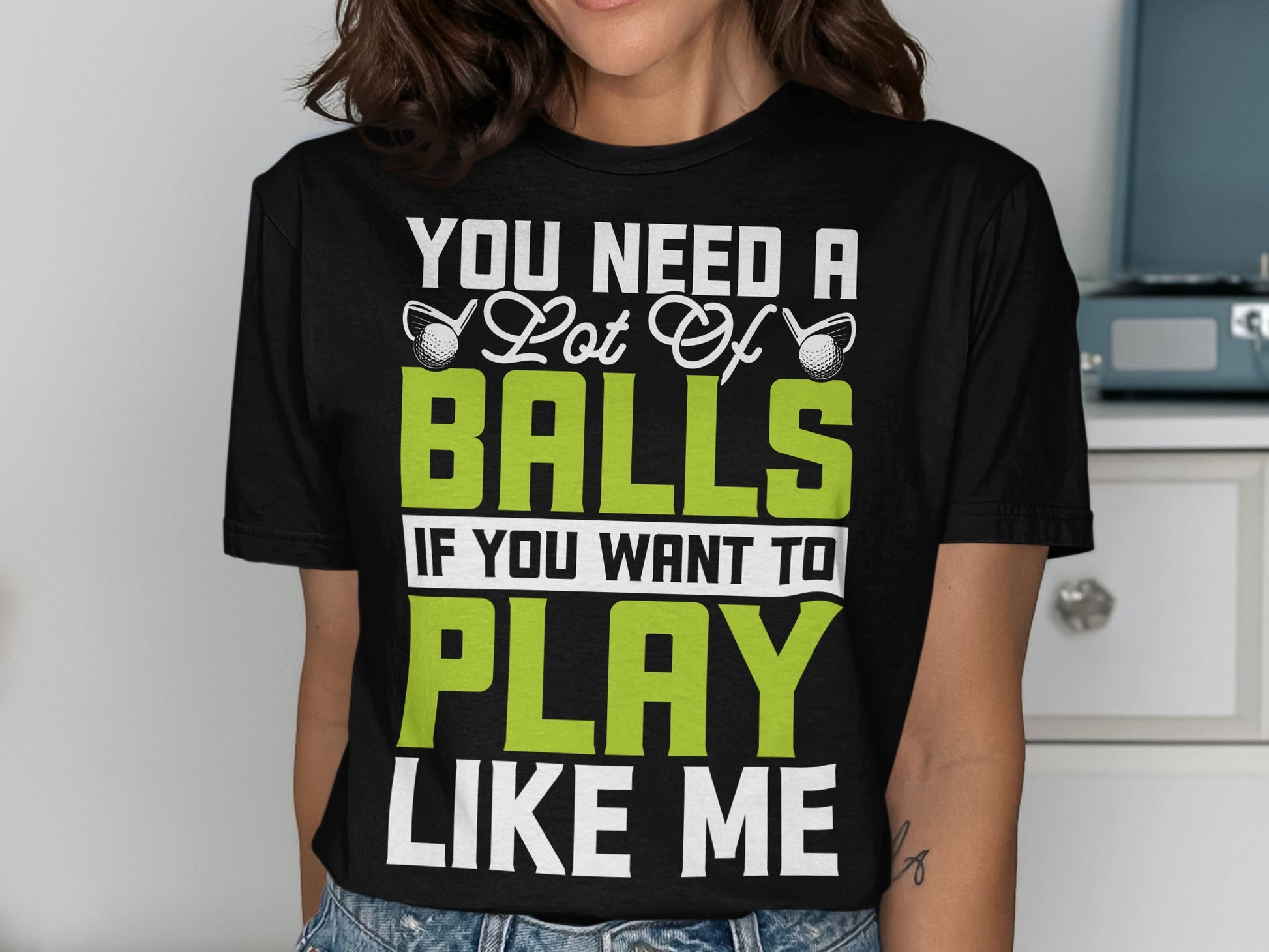 Black t-shirt with white text "You Need a Lot of Balls" and green text "PLAY LIKE ME".