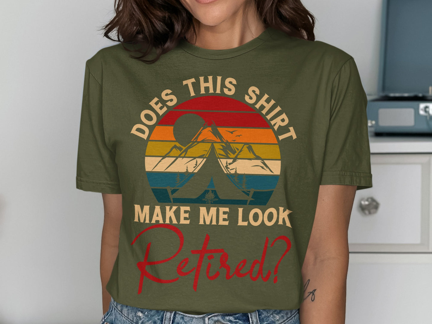 Olive green t-shirt with a sunset, tent, and mountains design and "DOES THIS SHIRT MAKE ME LOOK RETIRED?" text.