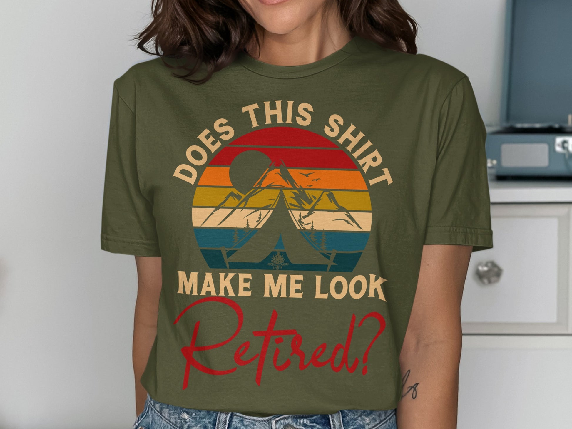 Olive green t-shirt with a sunset, tent, and mountains design and "DOES THIS SHIRT MAKE ME LOOK RETIRED?" text.