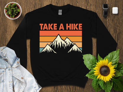 Black crewneck sweatshirt with mountains and retro stripes, "TAKE A HIKE" text.