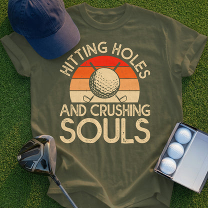 Olive green t-shirt with "Hitting Holes And Crushing Souls" and golf ball sunset graphic.