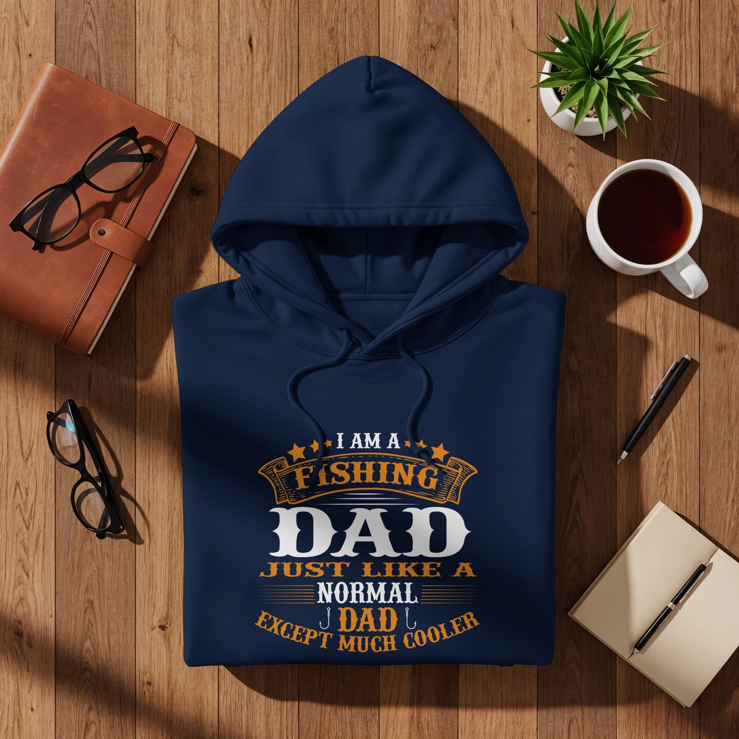 Navy hoodie with "Fishing Dad Except Much Cooler" text, flat lay on wood.