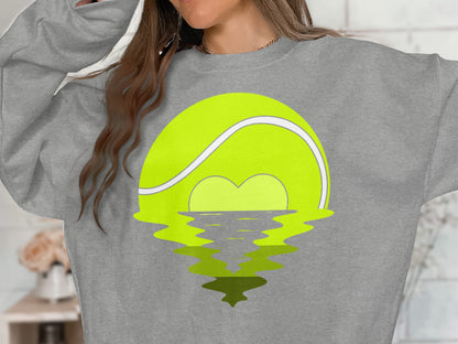 Tennis ball with heart-shaped sunset reflecting on water.