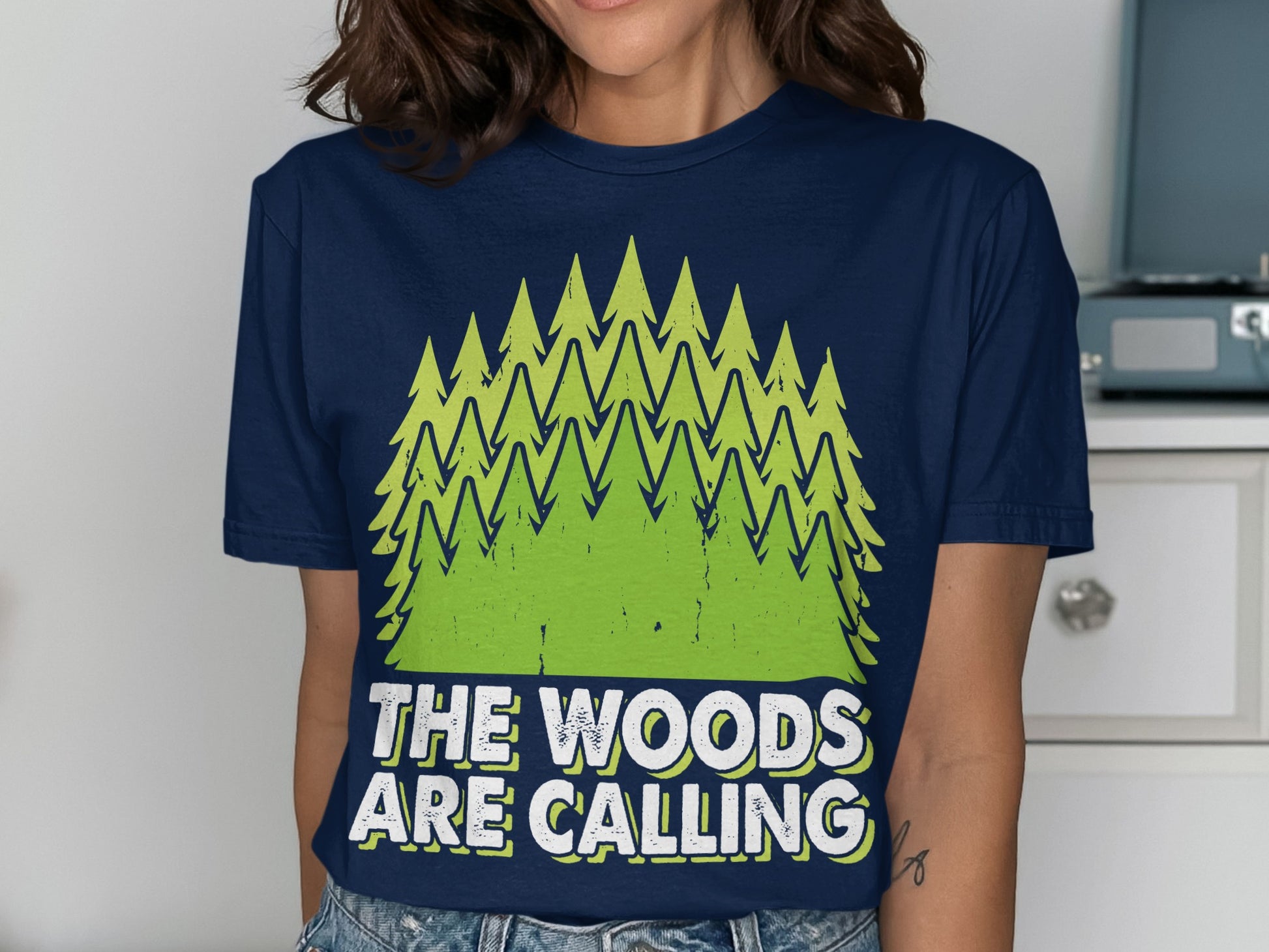 Navy t-shirt with green pine trees and text reading "The Woods Are Calling."