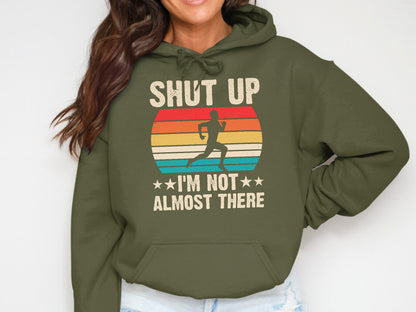 Green hoodie with runner silhouette and sunset graphic, text "SHUT UP I'M NOT ALMOST THERE".