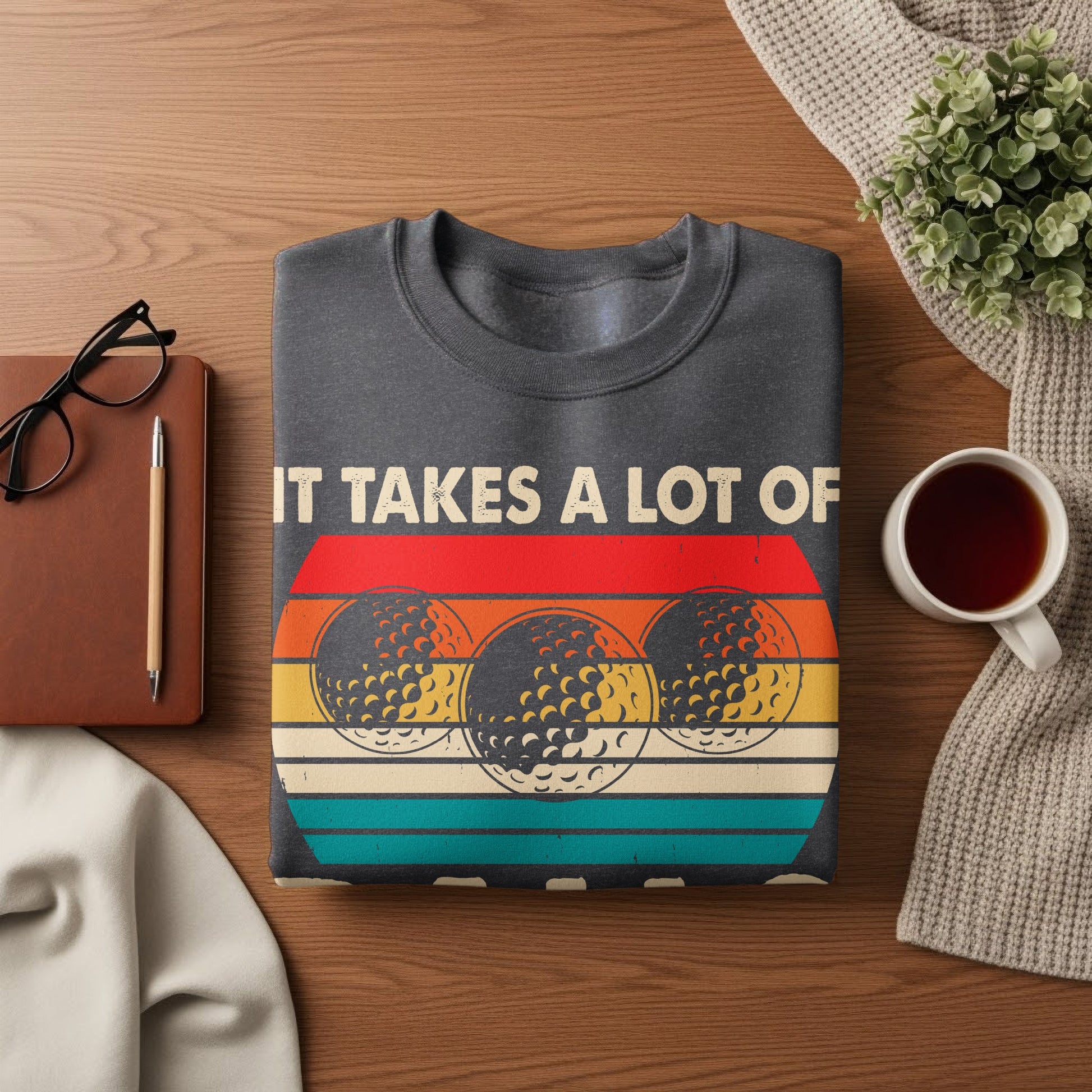 Dark gray sweatshirt with a retro design of three golf balls and text that reads "IT TAKES A LOT OF".