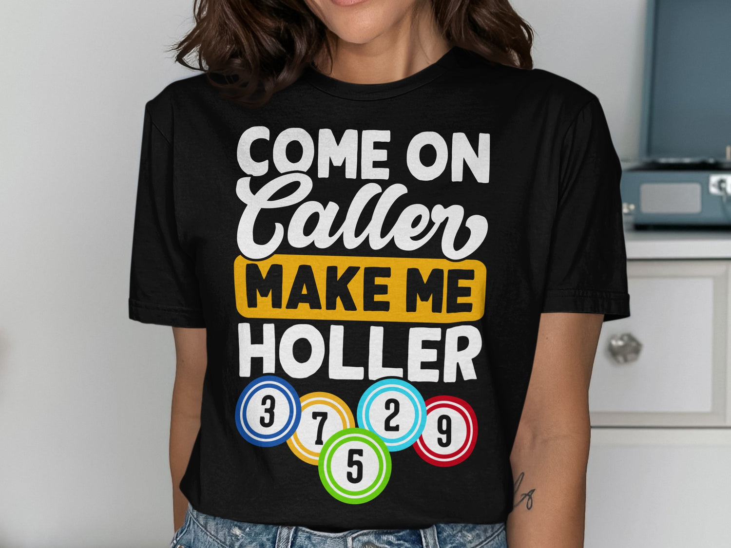 Black t-shirt with text "COME ON CALLER MAKE ME HOLLER" and colorful bingo balls.