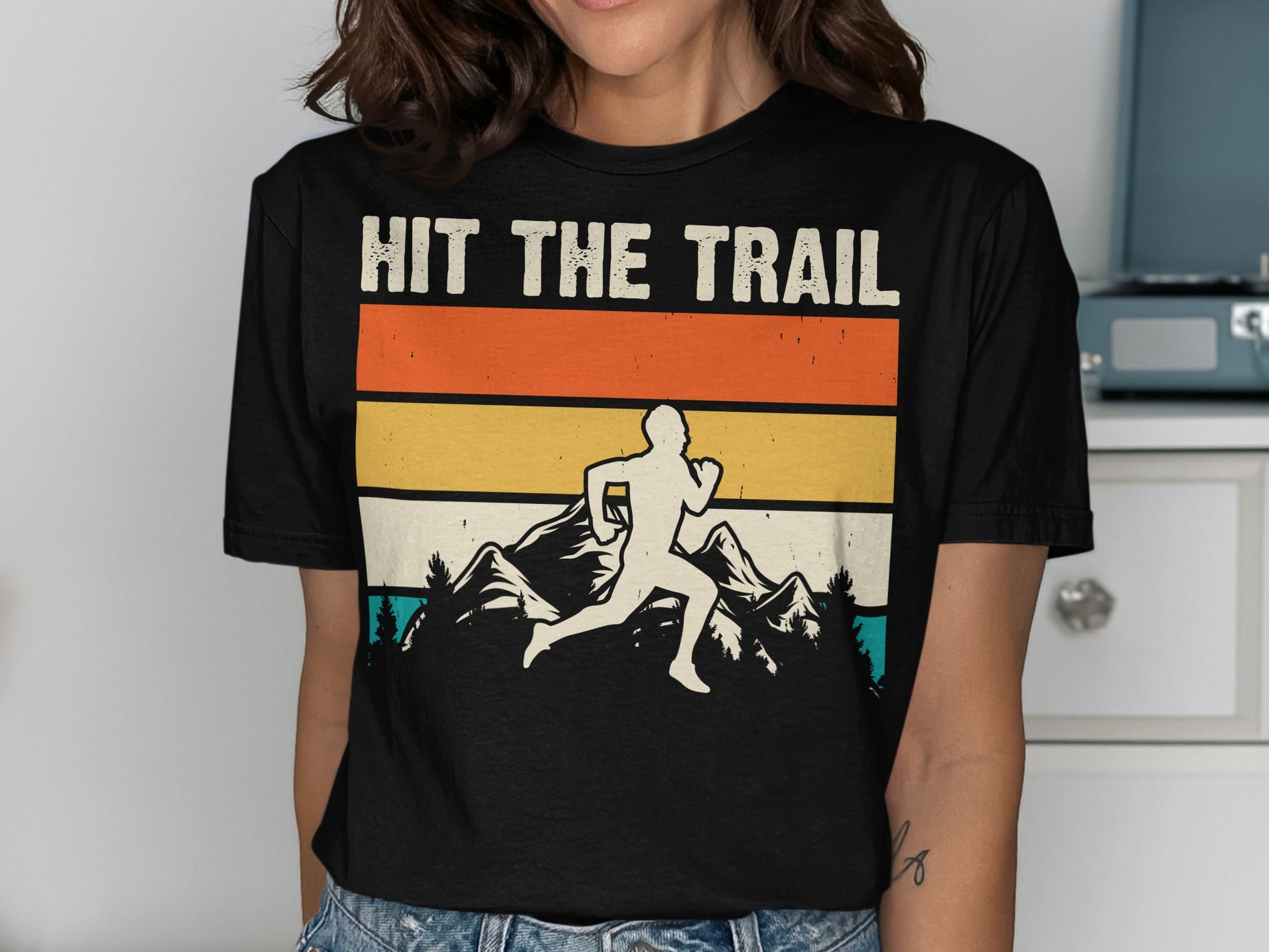 Black t-shirt with graphic of runner on mountain trail, text "HIT THE TRAIL".