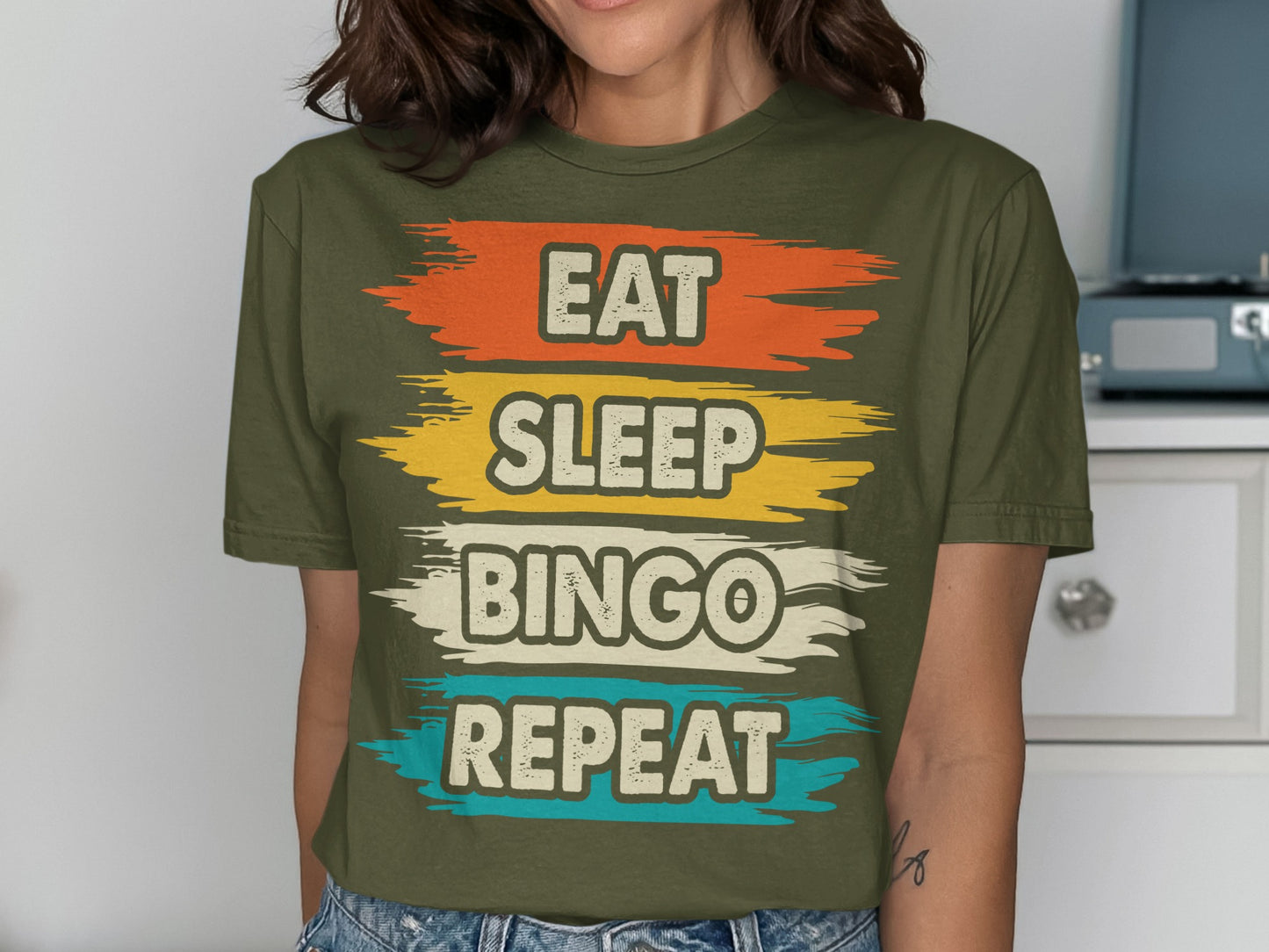 Olive green t-shirt with "EAT SLEEP BINGO REPEAT" in distressed colorful block letters.