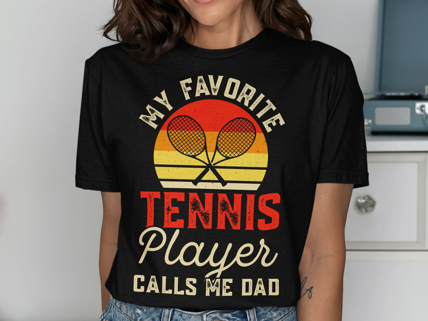 Black t-shirt with "MY FAVORITE TENNIS PLAYER CALLS ME DAD" graphic.