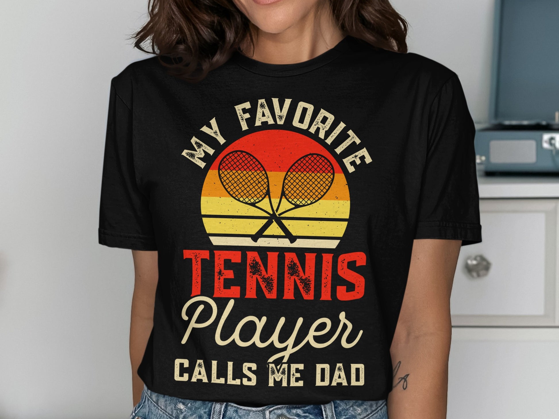 Black t-shirt with "MY FAVORITE TENNIS PLAYER CALLS ME DAD" graphic.