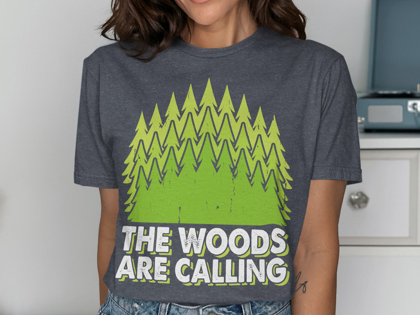 Dark grey t-shirt with green trees and text "THE WOODS ARE CALLING".