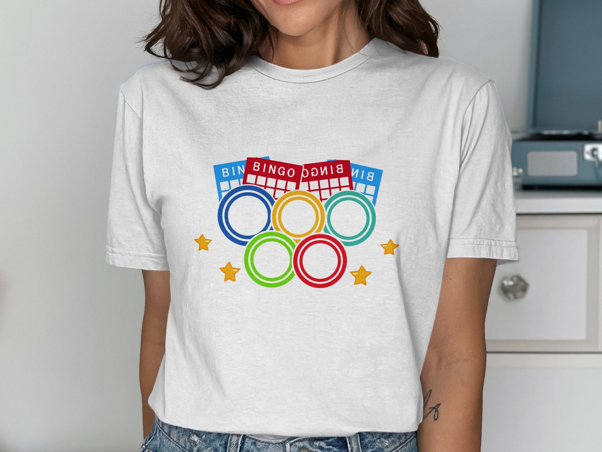 White t-shirt with bingo balls and Olympic rings graphic.