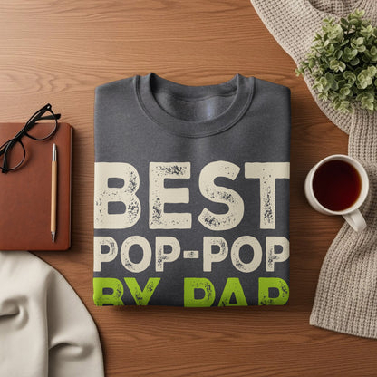 Dark gray sweatshirt with "BEST POP-POP" in cream and "BY DAD" in green text.