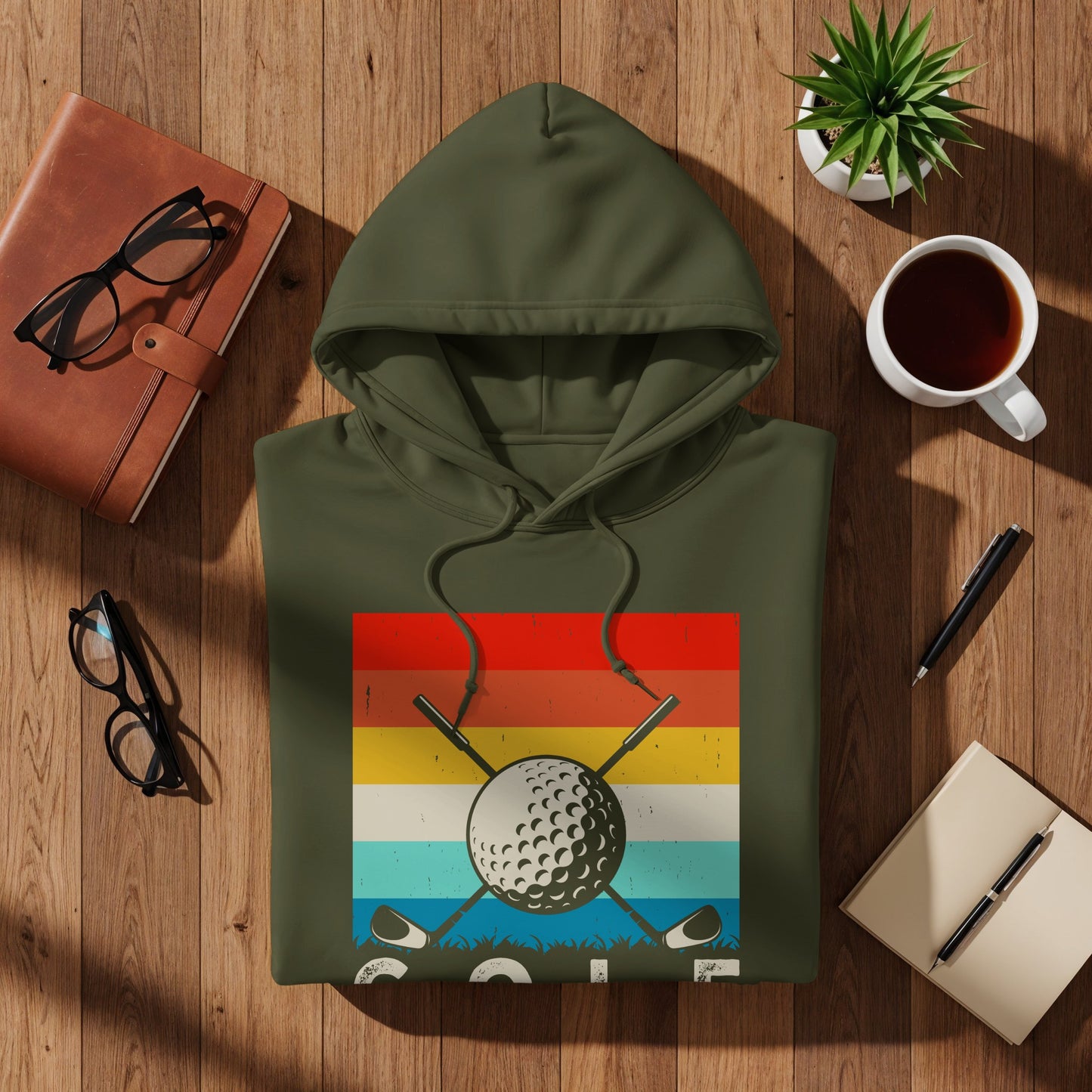 Olive green hoodie with a vintage golf graphic on a wooden surface.