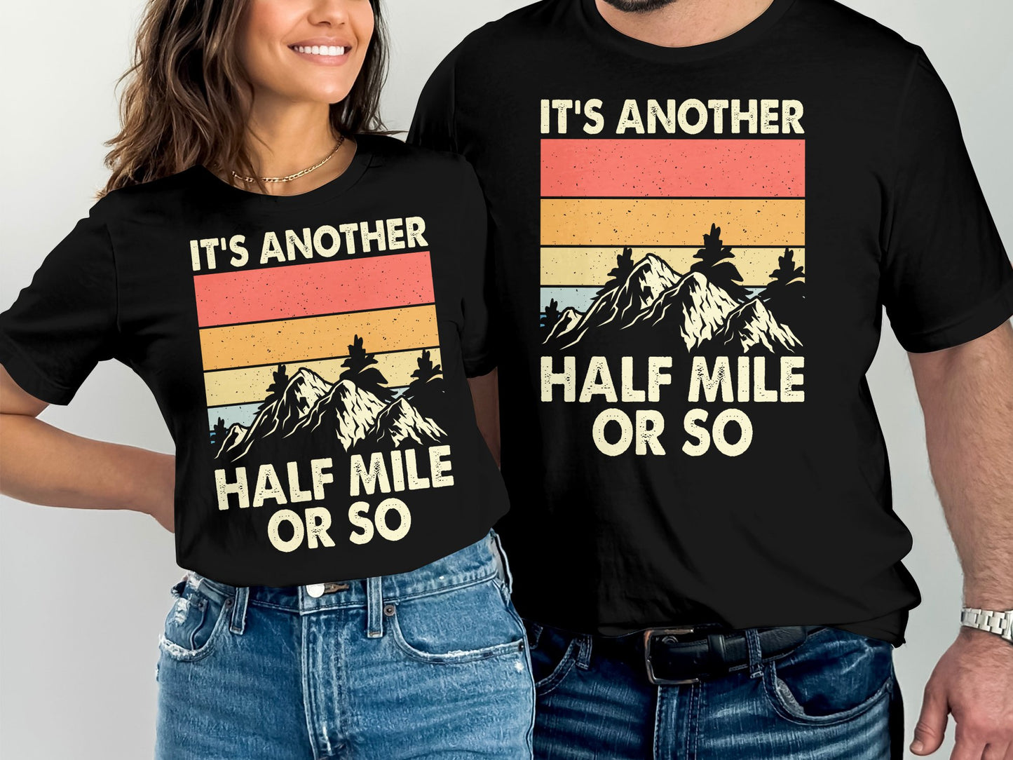 Two black t-shirts with mountain graphic and "It's another half mile or so" text.