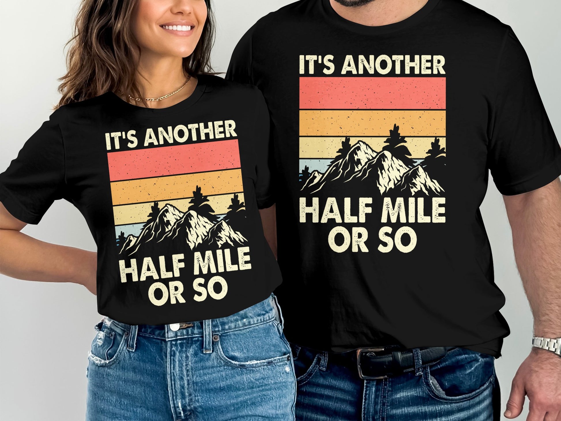 Two black t-shirts with mountain graphic and "It's another half mile or so" text.