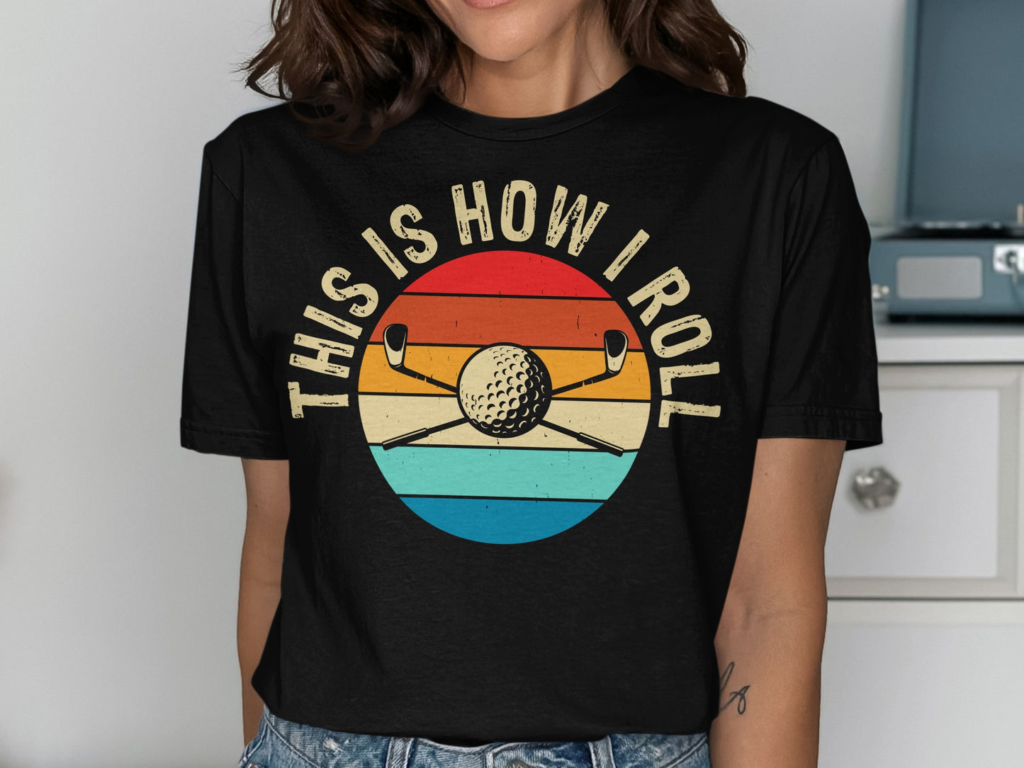 Black t-shirt with graphic: golf clubs and ball on retro sun design, text "THIS IS HOW I ROLL".