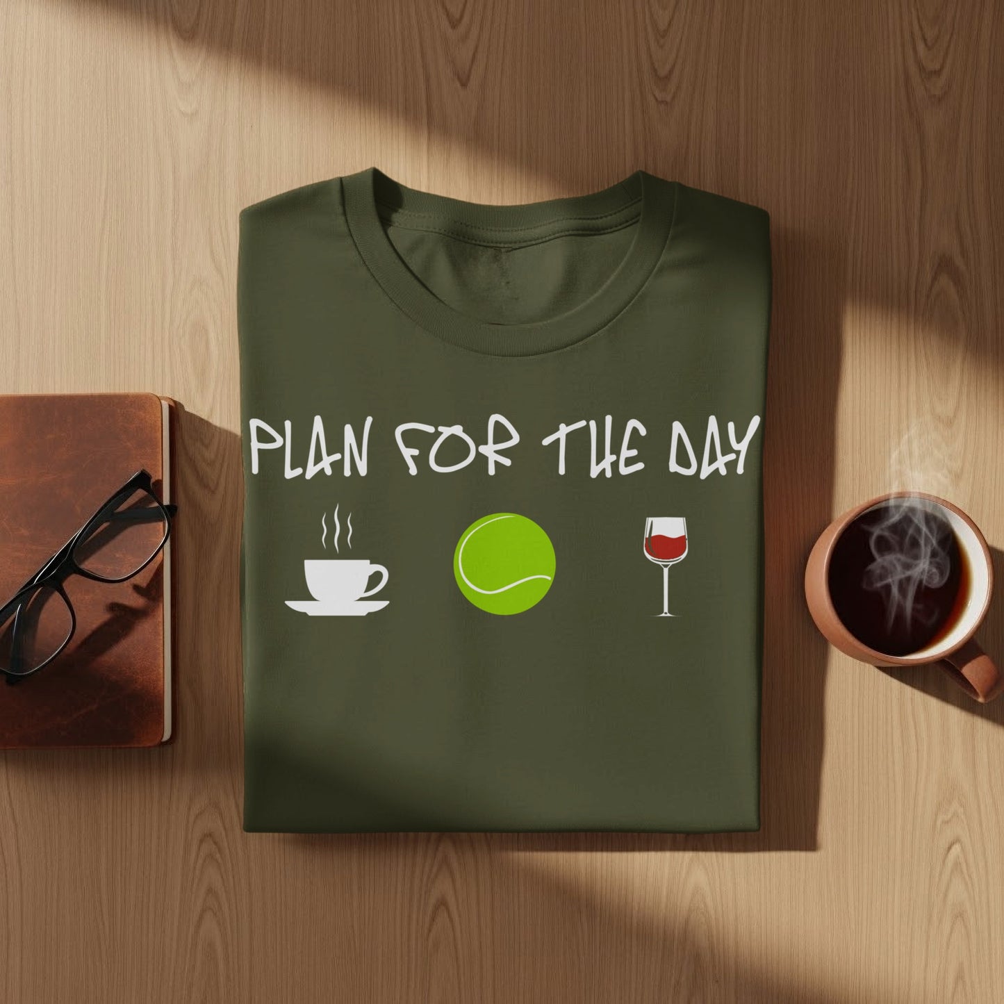 Olive green t-shirt with "Plan for the Day" text, coffee, tennis ball, and wine glass icons.