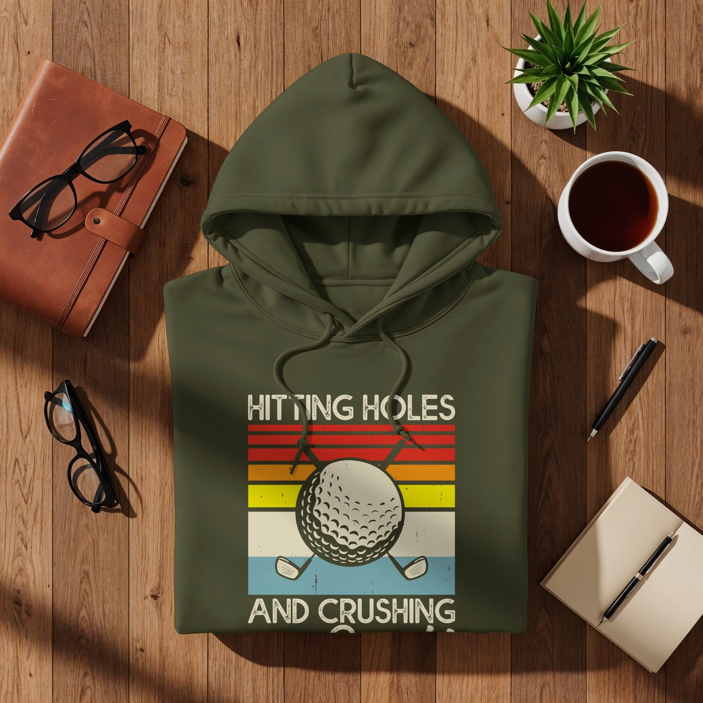 Olive green hoodie with "HITTING HOLES AND CRUSHING" text and golf ball graphic.