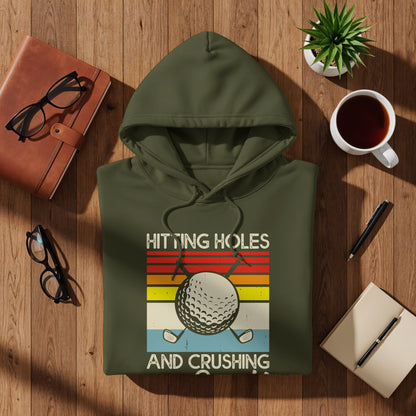 Olive green hoodie with "HITTING HOLES AND CRUSHING" text and golf ball graphic.
