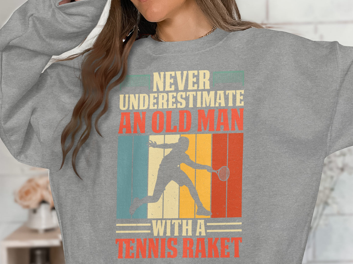 Gray sweatshirt with "Never Underestimate an Old Man with a Tennis Racket" text and retro graphic.