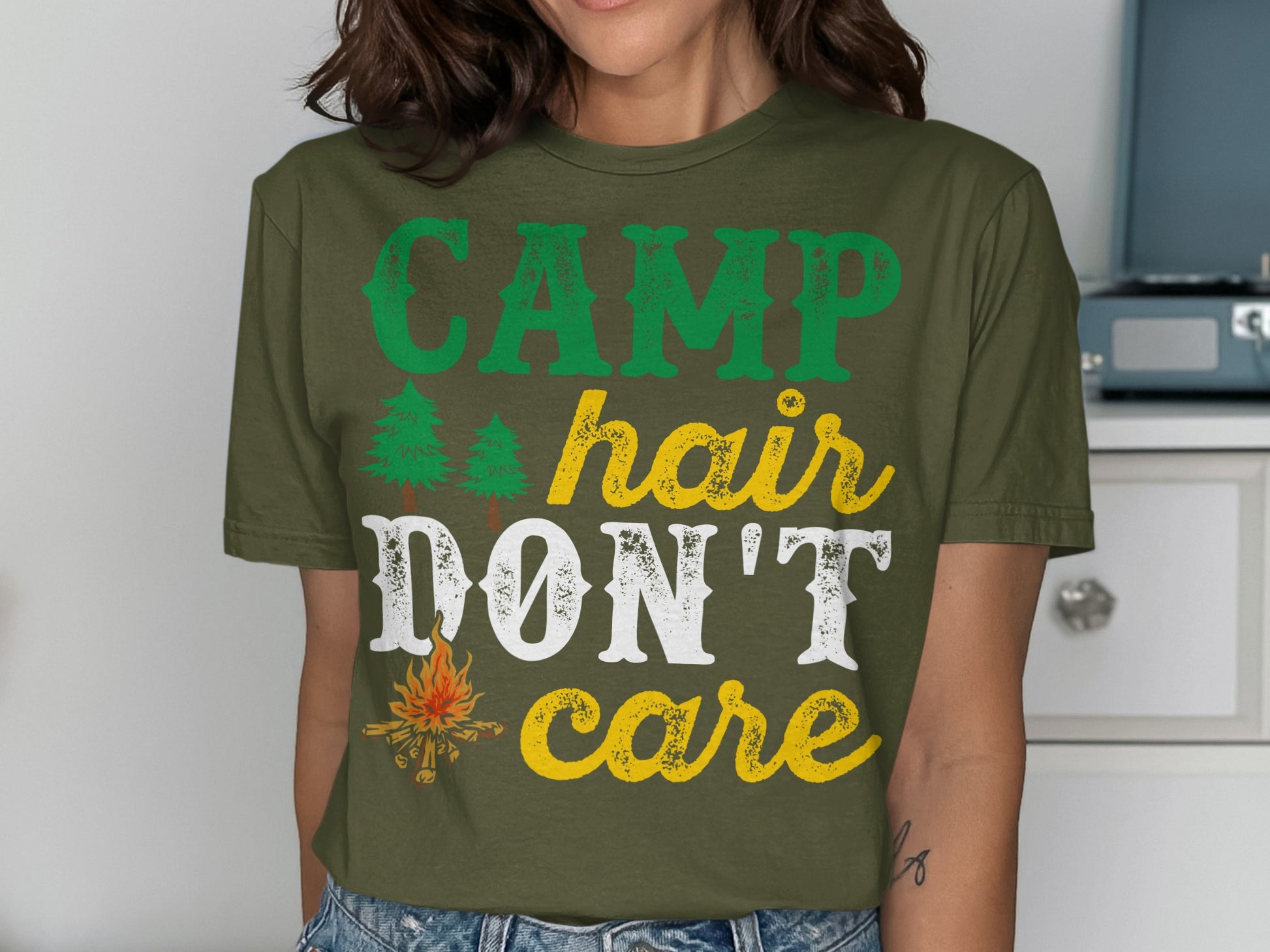 Green t-shirt with "CAMP hair DON'T care" text and small tree and campfire graphics.