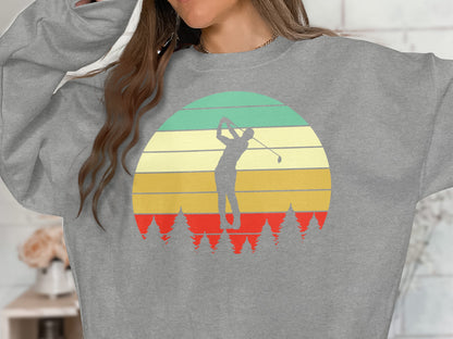 Gray sweatshirt with retro sunset, golfer silhouette, and pine trees graphic.