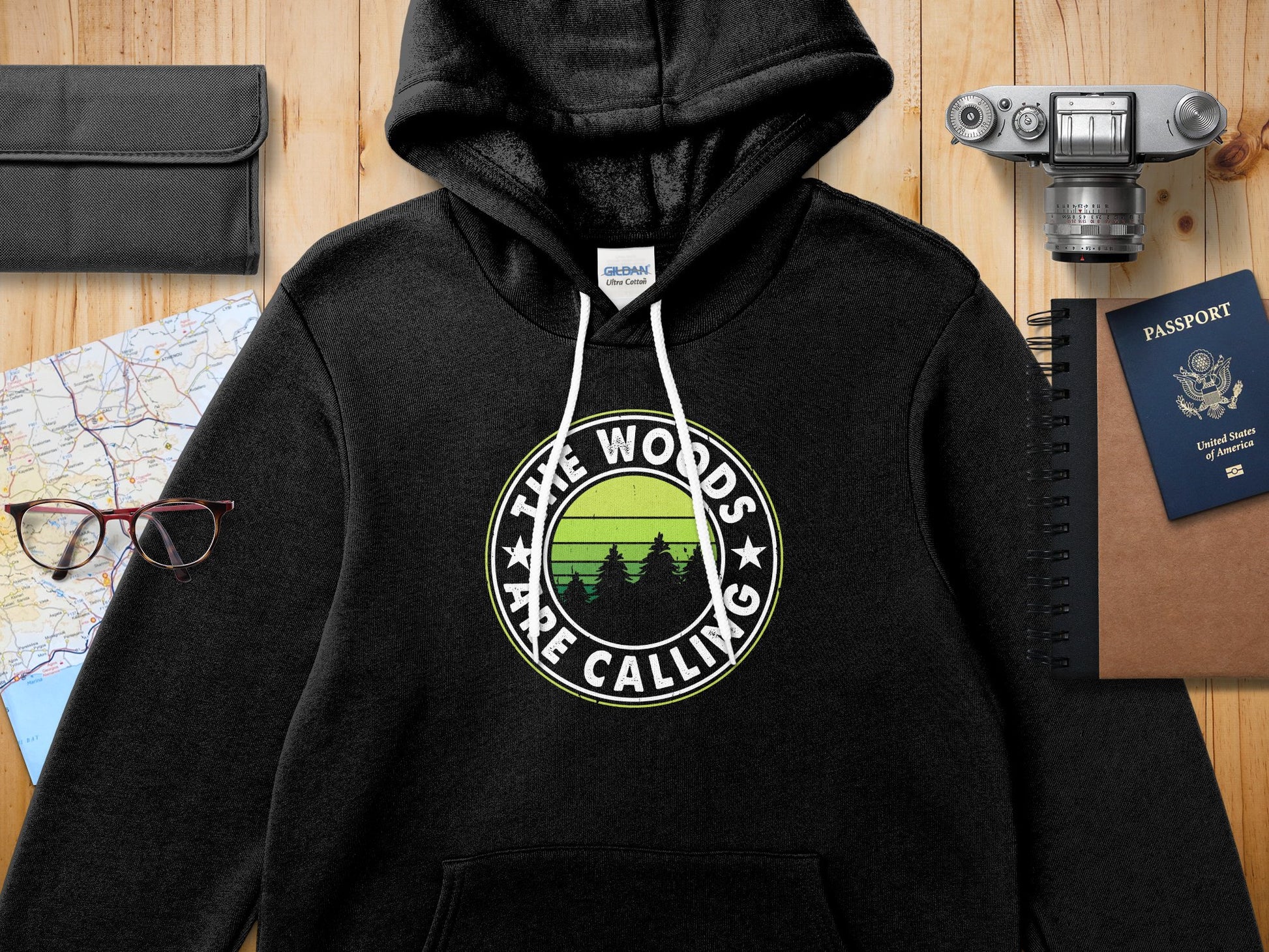 Black hooded sweatshirt with "The Woods Are Calling" text and forest graphic.