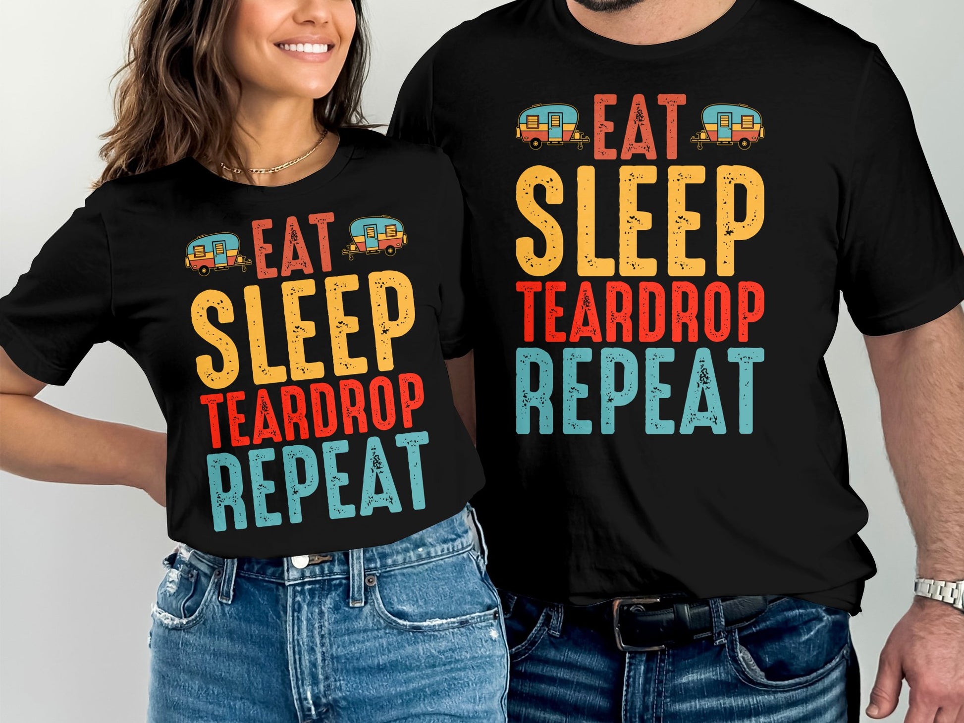 Couple wearing black t-shirts with "Eat Sleep Teardrop Repeat" and caravan graphics.