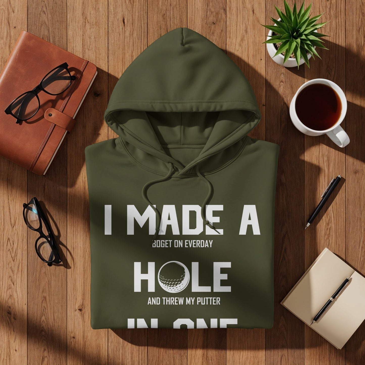 Olive green hoodie with "I MADE A HOLE IN ONE" text and golf ball graphic.