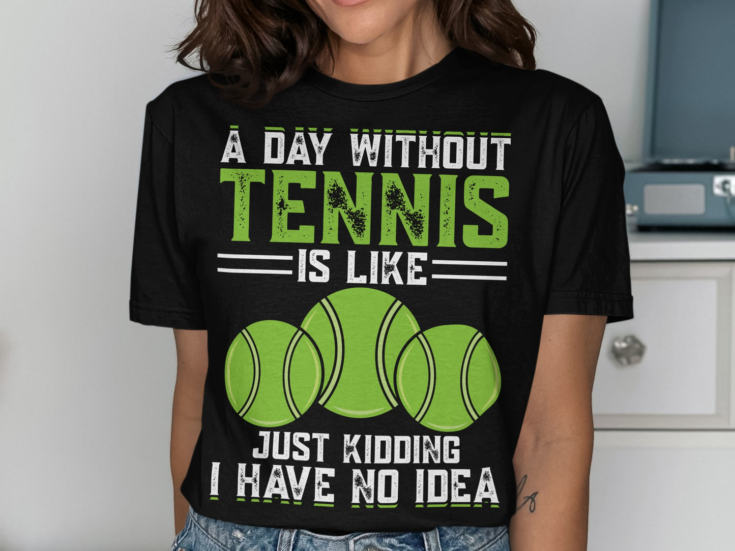 Black t-shirt with text "A DAY WITHOUT TENNIS IS LIKE JUST KIDDING I HAVE NO IDEA" and three tennis balls.