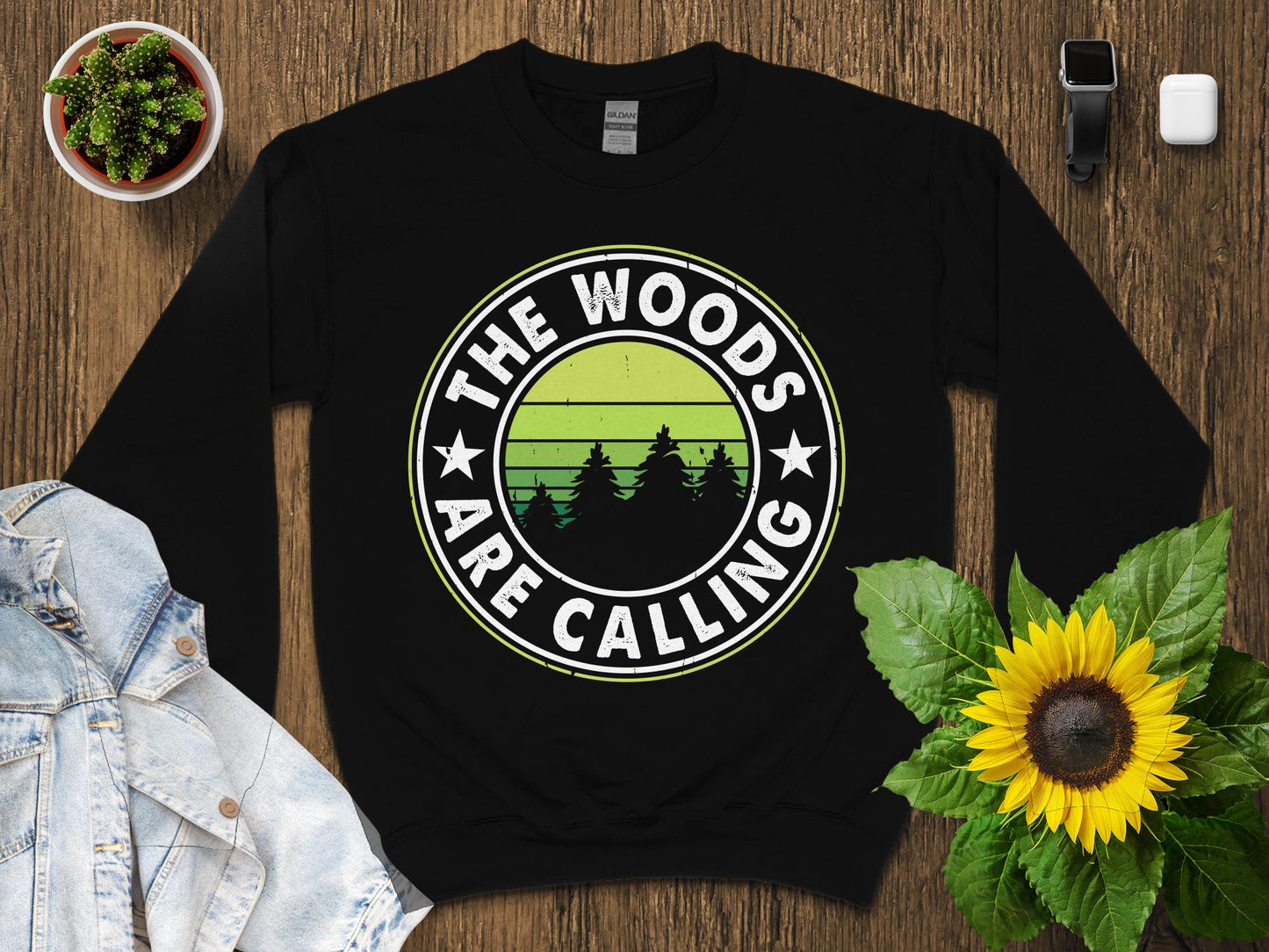 Black sweatshirt with "The Woods Are Calling" text and a green forest graphic.