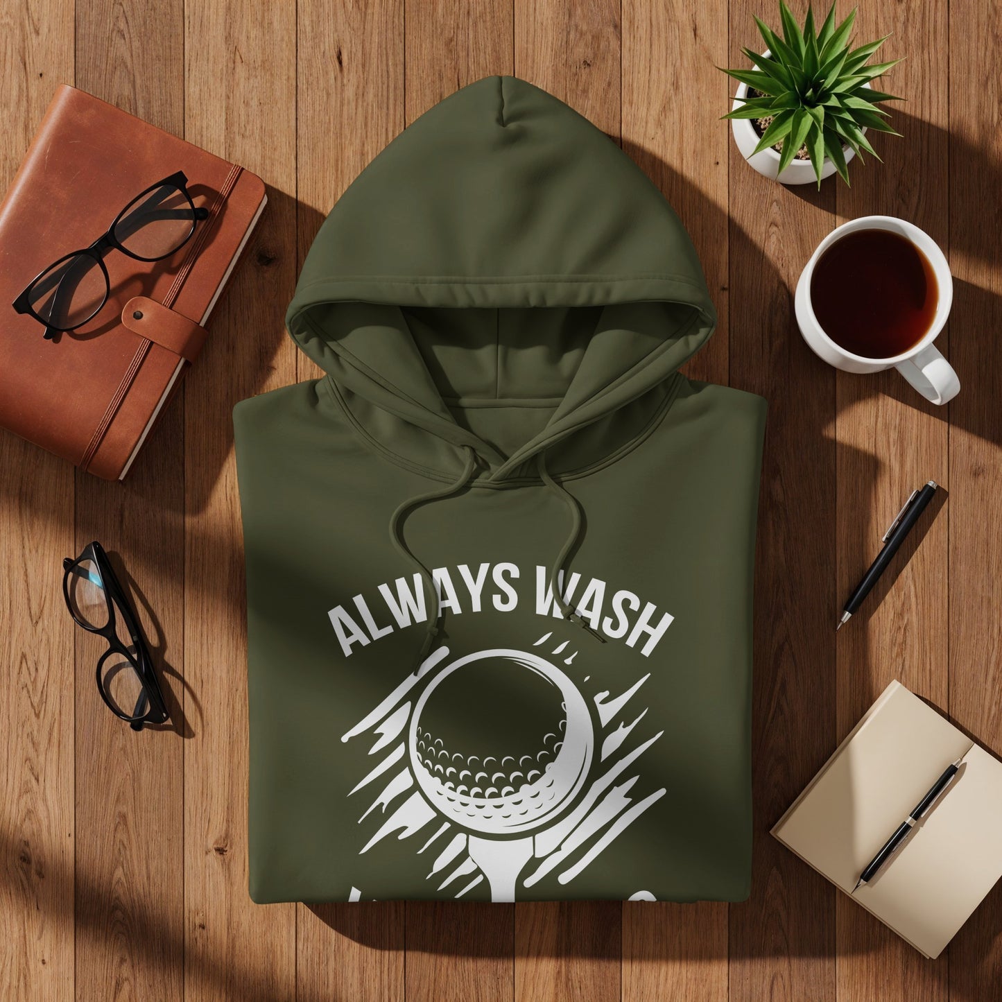 Green hoodie with "Always Wash" and golf ball graphic on a wooden surface.
