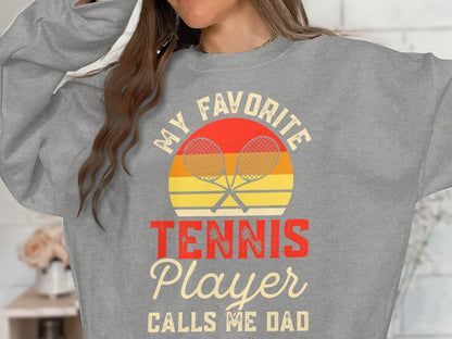 Gray sweatshirt with "MY FAVORITE TENNIS PLAYER CALLS ME DAD" text and crossed racquets.