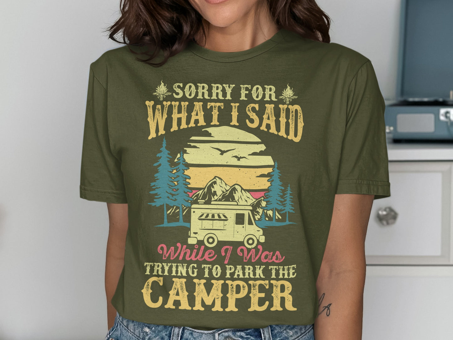 Olive green t-shirt with "Sorry for what I said while parking the camper" text and mountain scene.