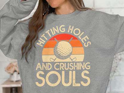 Gray sweatshirt with a graphic of a golf ball and crossed clubs with sunset stripes.