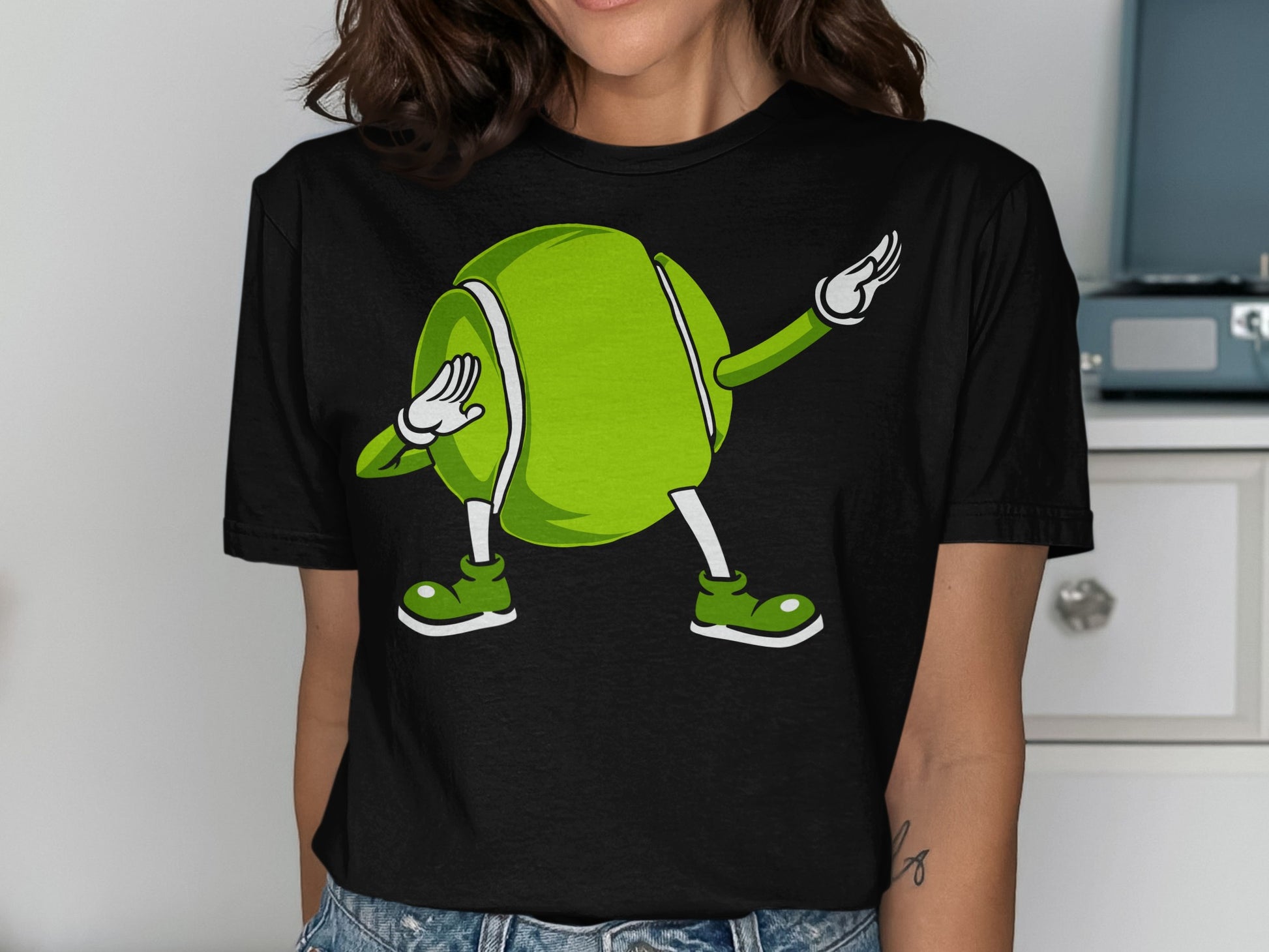 Cartoon tennis ball character dabbing on a black t-shirt.