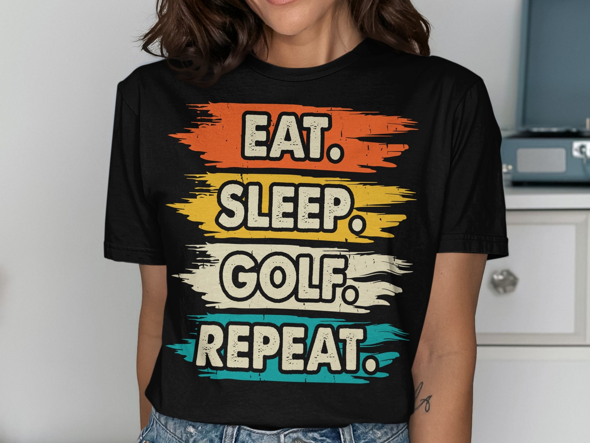 Black t-shirt with "Eat. Sleep. Golf. Repeat." text in distressed colorful stripes.