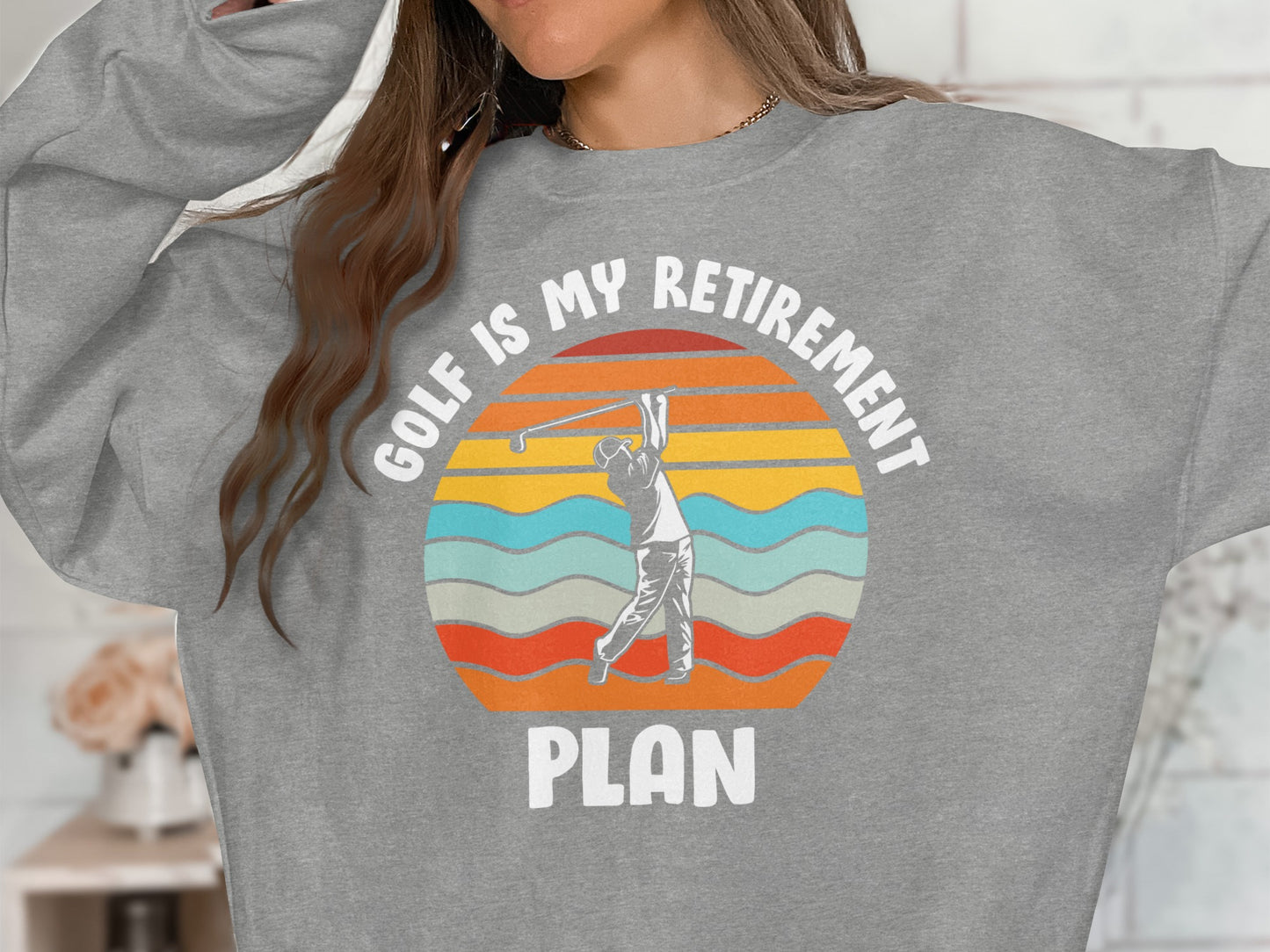 Gray sweatshirt with "Golf is my retirement plan" text and a sunset graphic.
