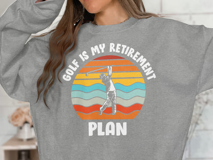 Gray sweatshirt with "Golf is my retirement plan" text and a sunset graphic.
