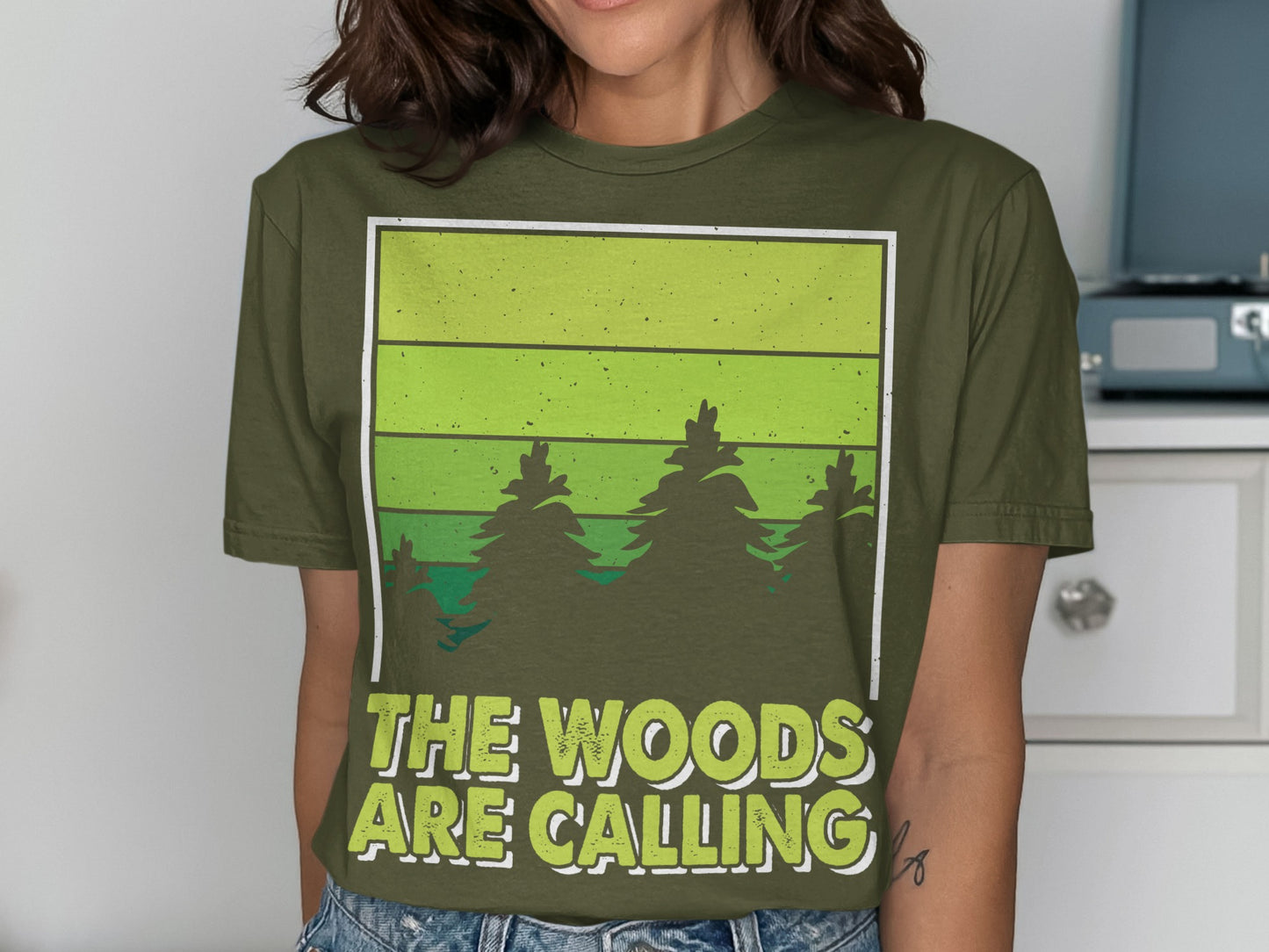 Green t-shirt with forest graphic and "THE WOODS ARE CALLING" text.