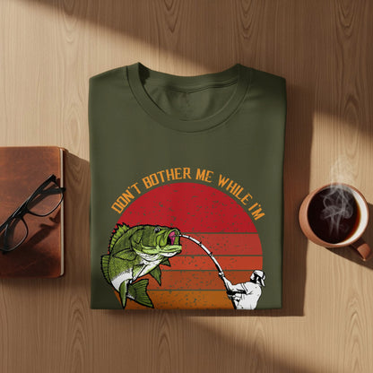 Green t-shirt with text "Don't bother me while I'm fishing" and a graphic of a fisherman catching a bass.