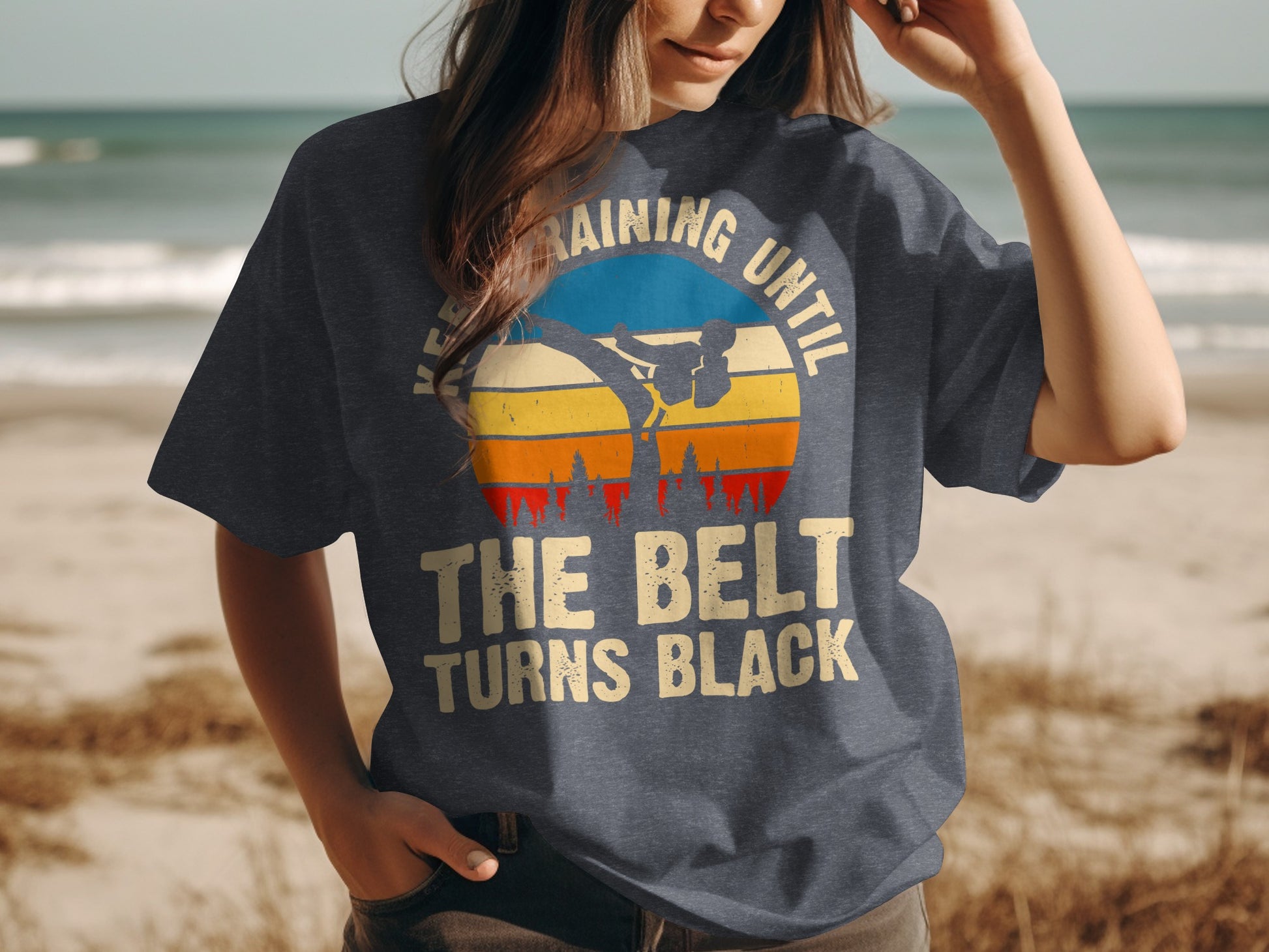 T-shirt with graphic of martial artist silhouetted against a sunset, text "TRAINING UNTIL THE BELT TURNS BLACK".